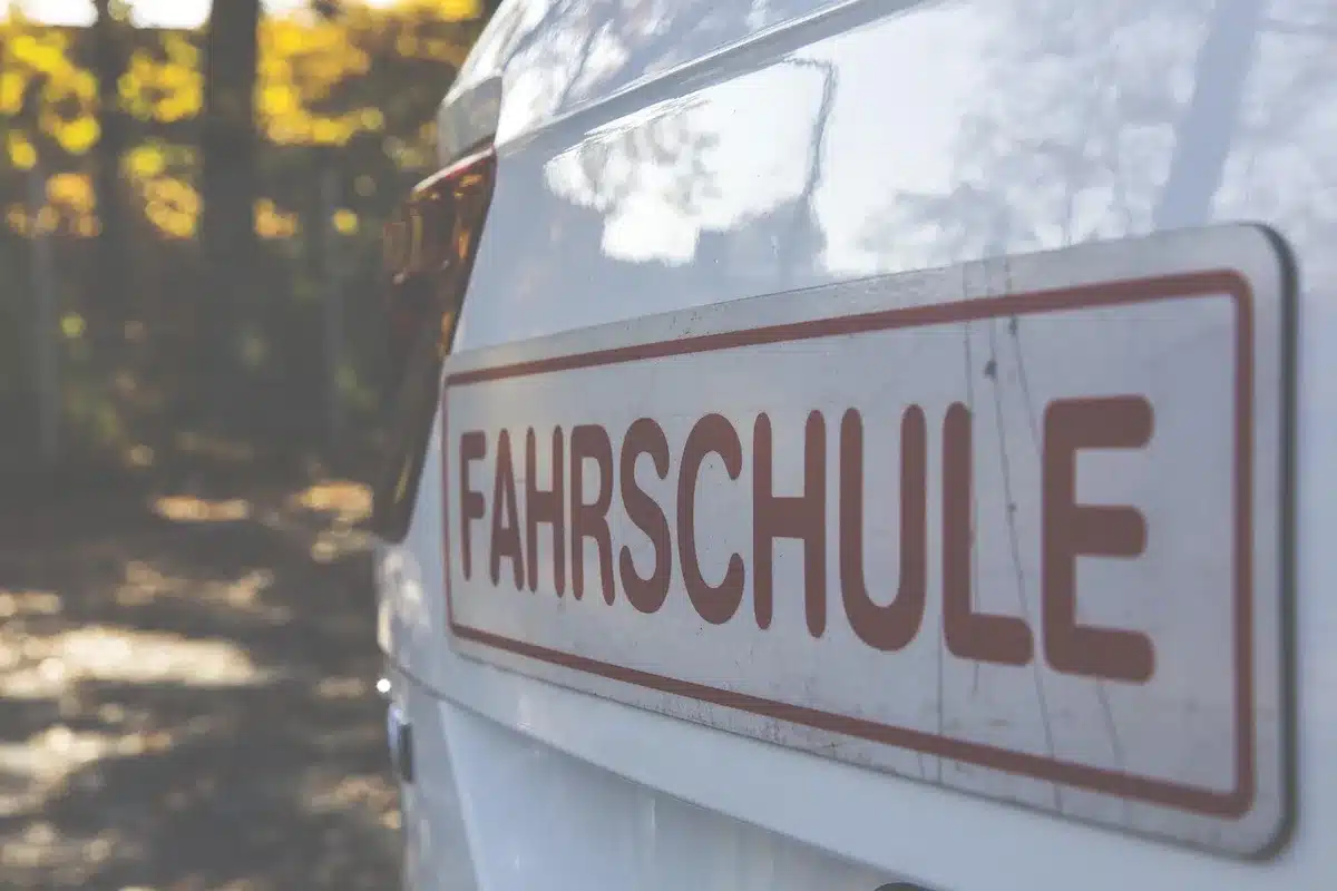 Naheinstellung: Hände halten einen Führerschein-Ersatz neben Münzstapel und Lehrbuch auf einem Tisch